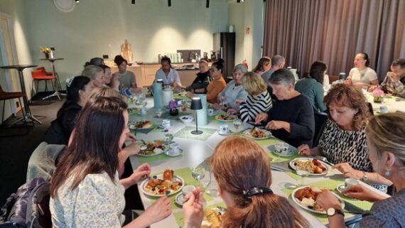 En gruppe ansatte sitter rundt et langbord og nyter et måltid sammen i et lyst rom med moderne innredning på Betanien rehabilitering. Tallerkener med mat, kopper og glass står på bordet og skaper en sosial og avslappet atmosfære.