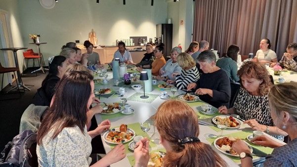 En gruppe ansatte sitter rundt et langbord og nyter et måltid sammen i et lyst rom med moderne innredning på Betanien rehabilitering. Tallerkener med mat, kopper og glass står på bordet og skaper en sosial og avslappet atmosfære.