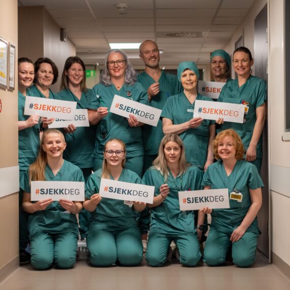 En gruppe helsearbeidere i unifrom står i en gang på Betanien sykehus med skilt med påskriften #sjekkdeg.