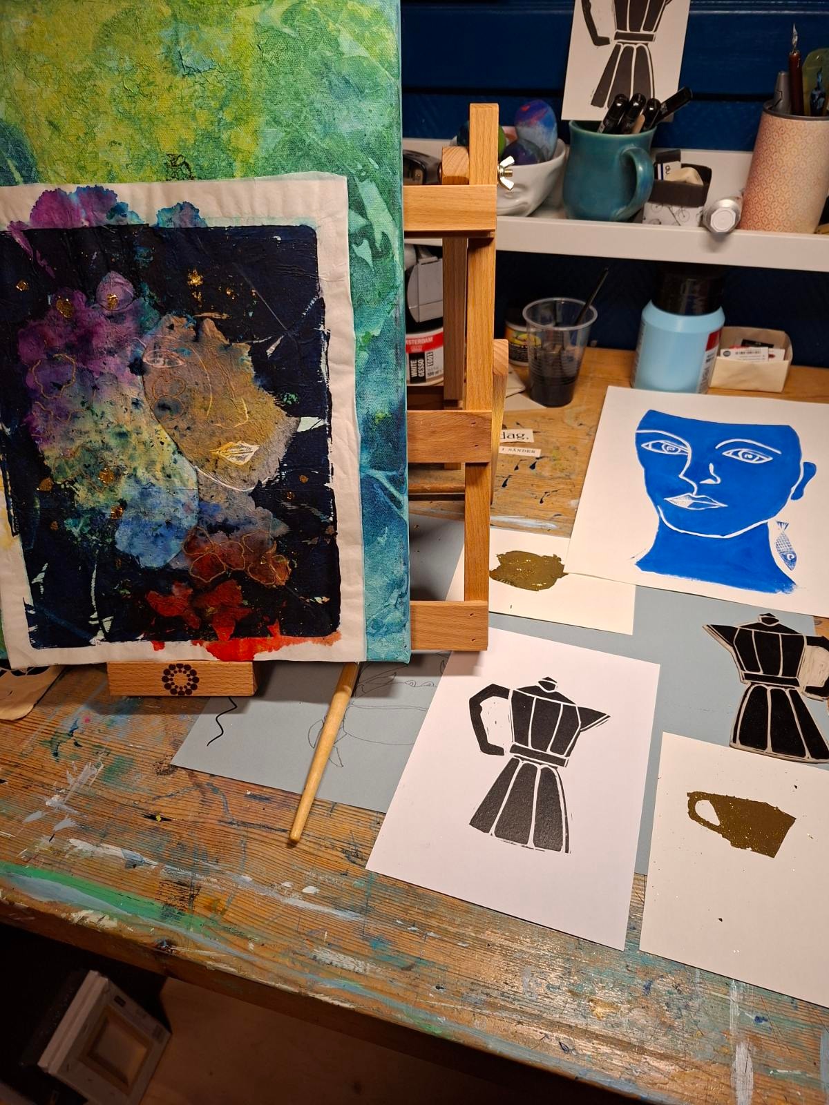 Et trebord med kunstartikler, et lite staffeli med et fargerikt, abstrakt maleri og flere trykk - ett med Betanien sykehus - viser 25 års kreativitet inspirert av jobbe med mennesker.