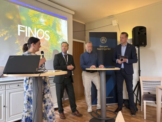 Fire personer står og snakker på et frokostmøte innendørs, med en FINOS-presentasjonsskjerm og et banner fra Bergen Næringsråd synlig i bakgrunnen.